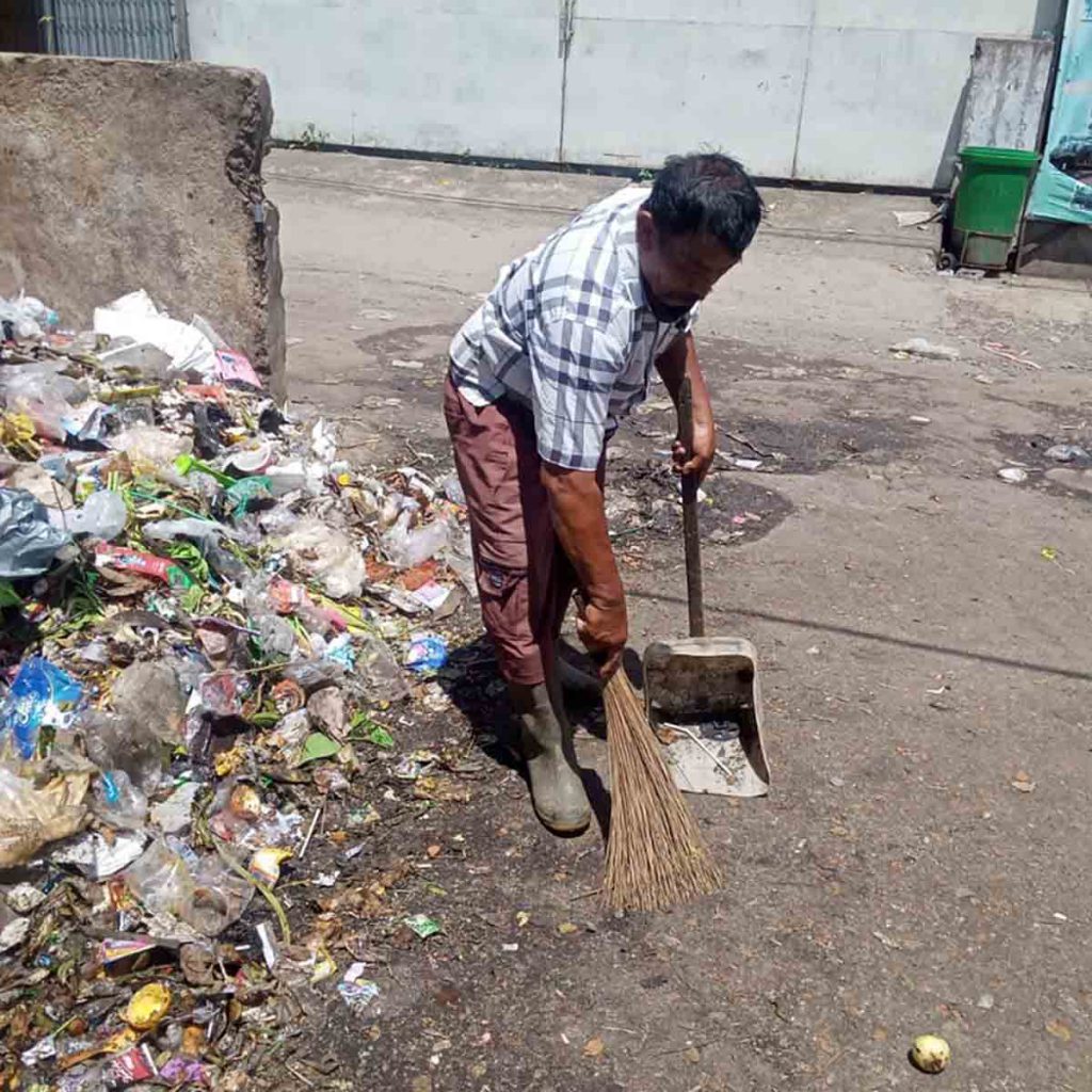 Petugas jaga piket TPS Pasar Genteng II membersihkan sampah yang bertebaran di jalan raya