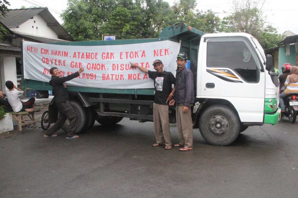 BLOKADE JALAN - Warga Desa Kemiri, Kecamatan/Kabupaten Sidoarjo memblokade jalan menggunakan truk dan memasang spanduk penolakan rencana penyitaan aset desa mereka, Selasa (15/12/2020) - Warga Kemiri Ngotot Pertahankan Aset Desa