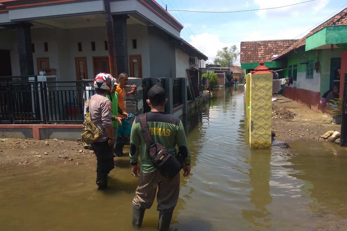 TERJUN LOKASI: Anggota Polsek Tanggulangin yang diterjunkan ke lokasi terdampak banjir, Aipda Puput ardianto membantu warga membuat saluran air. (gus) - Polsek Tanggulangin Terjunkan Personel Antisipasi Banjir
