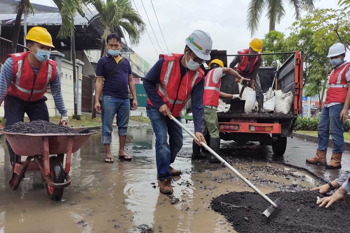 PERBAIKAN - Plt Camat Buduran, Aan Alifauzansyah ikut menambal jalan rusak yang ada di Perumahan Pondok Jati Desa Pagerwojo, Kecamatan Buduran, Sidoarjo menggunakan aspal Asbuton, Sabtu (06/03/2021) - Perbaikan Jalan Pakai Aspal Asbuton - Hujan Tidak Jadi Penghalang