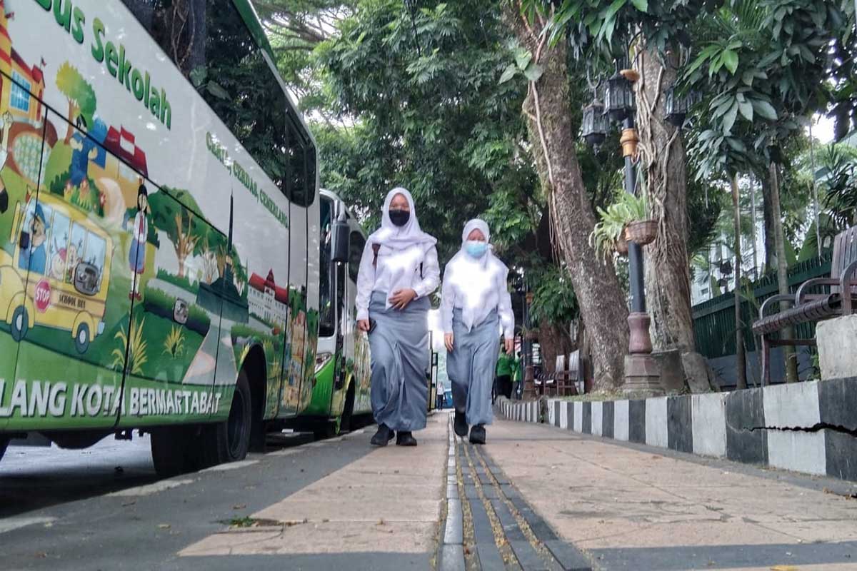 Dua siswi sedang berjalan di trotoar dekat dekat Bundaran Tugu Malang. (jaz) - Siswa Kota Malang Antusias Ikuti PTM Uji Coba Daripada Daring