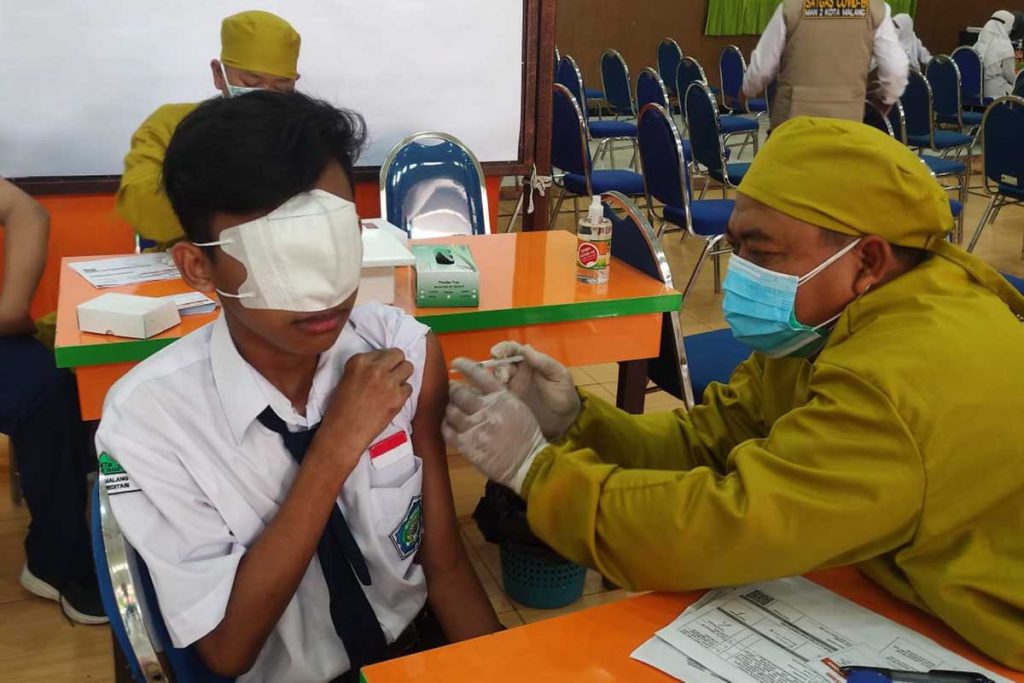 Salah satu siswa menutup mata dengan masker lantaran takut jarum. (rhd) - 2000 Siswa Madrasah se-Kota Malang Divaksin Sinovac - MTsN 1 Kota Malang Hampir 100 Persen Herd Immunity