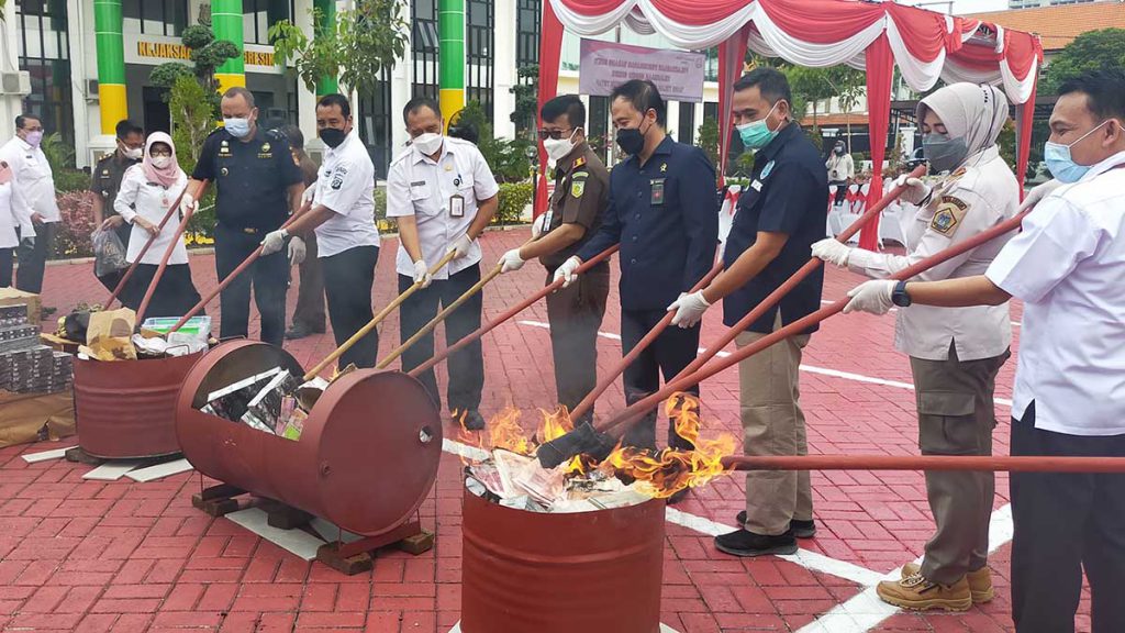 PEMUSNAHAN : Kejari Gresik bersama Bea Cukai dan APH terkait melakukan pembakaran dan pemusnahan rokok ilegal - Kejari Gresik dan Bea Cukai Musnahkan 106,8 Ribu Batang Rokok Tanpa Cukai - Rugikan Negara Hingga Rp 97 Juta