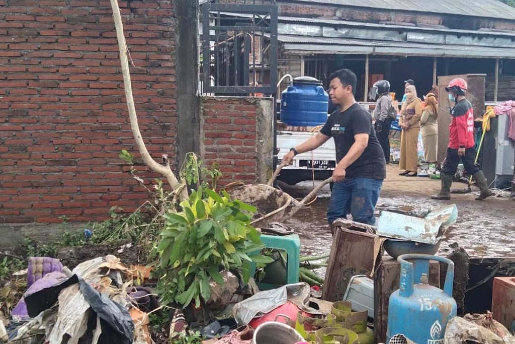 Salah satu warga sedang membersihkan kotoran lumpur pasca banjir luapan sungai. (jaz) - Trauma Pemilik Mobil Hanyut, Terjebak Banjir Naik Kanopi Rumah