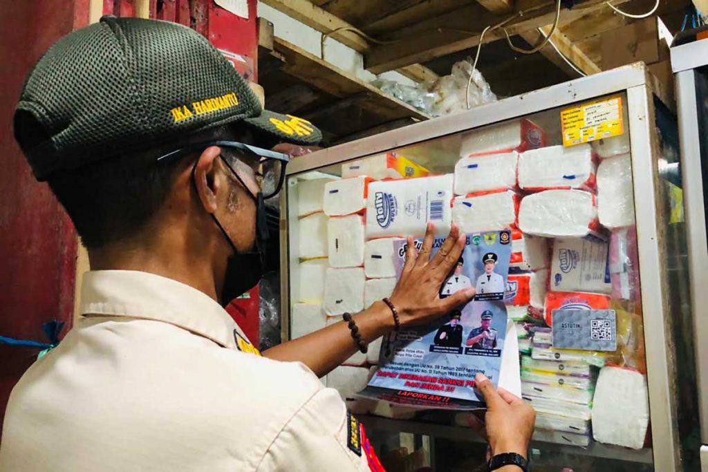Petugas Satpol PP memasang stiker Gempur Rokok Ilegal di salah satu toko Pasar Kromengan. (ws6) - Satpol PP Kabupaten Malang dan Bea Cukai Sobo Pasar Gempur Rokok Ilegal - Sobo Pasar Wonosari dan Kromengan