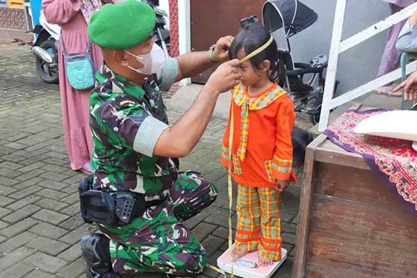 Babinsa Buring, Sertu Arief membantu pemeriksaan balita di posyandu. (ist) - Babinsa Kedungkandang Dampingi Pencegahan Stunting di Posyandu Buring