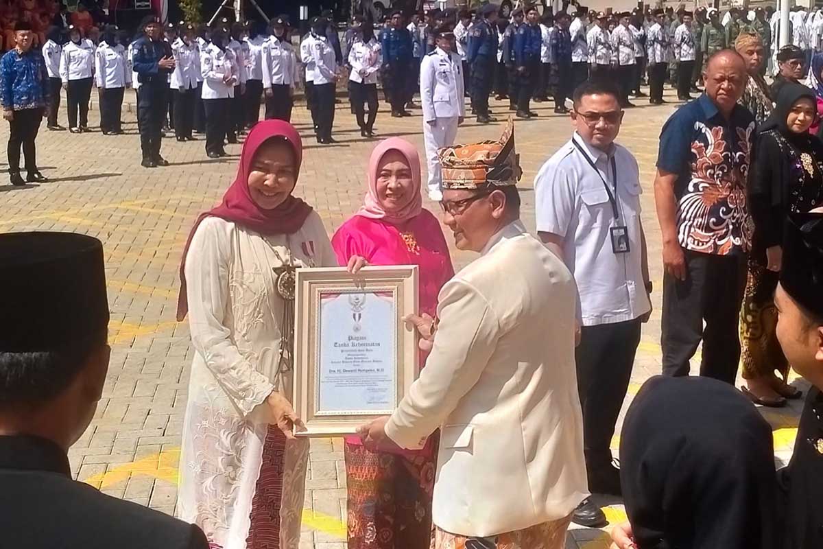 Dra Hj Dewanti Rumpoko menerima lencana emas dan penghargaan dari Pj Wali Kota Batu. (dik) - Spesial, Upacara HUT ke-22 Kota Batu Diperingati di Pasar Among Tani
