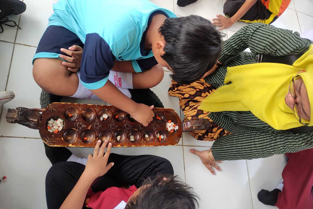 Dua siswa dipandu cara bermain dakon. (rhd) - Disdikbud Ajak Belajar Bersama dan Bermain Permainan Tradisional di Museum Pendidikan