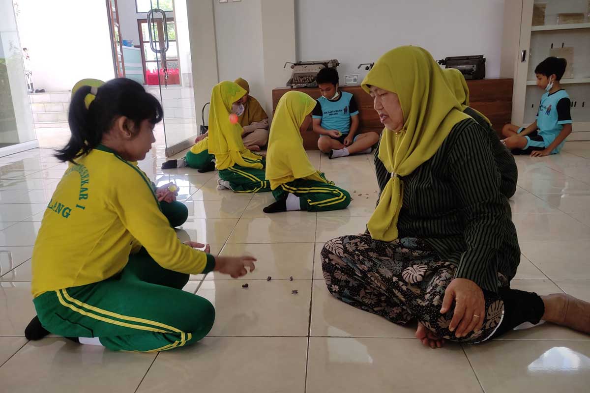 Staf Museum Pendidikan mengajari bagaimana cara bermain bola bekel. (rhd) - Disdikbud Ajak Belajar Bersama dan Bermain Permainan Tradisional di Museum Pendidikan