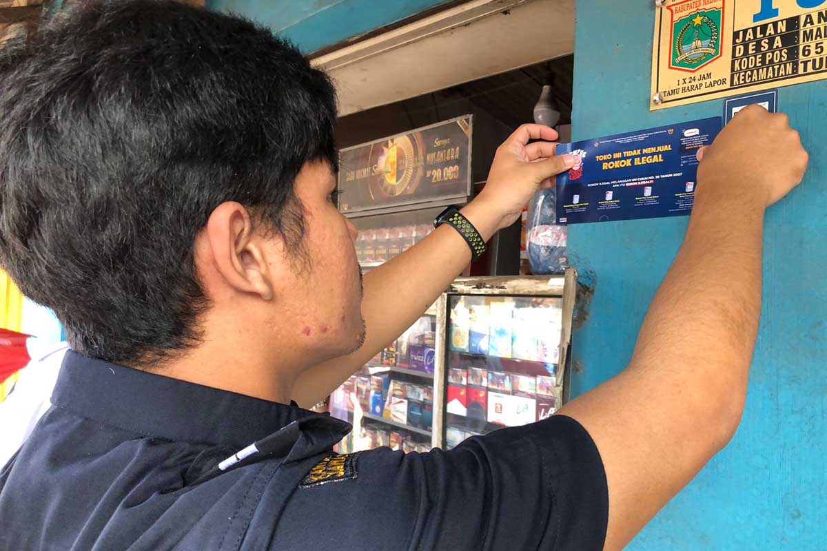 Penempelan stiker gempur rokok ilegal di salah satu toko di Kecamatan Tumpang. (wul) - Kecamatan Tumpang dan Poncokusumo, Jadi Sasaran Sosialisasi Gempur Rokok Ilegal